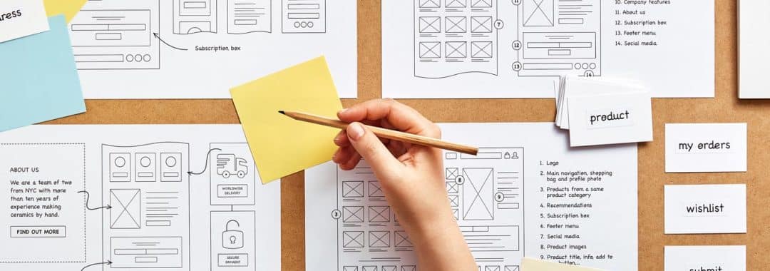 Flat lay image of numerous website wireframe sketches and card sorting technique over product designer desk